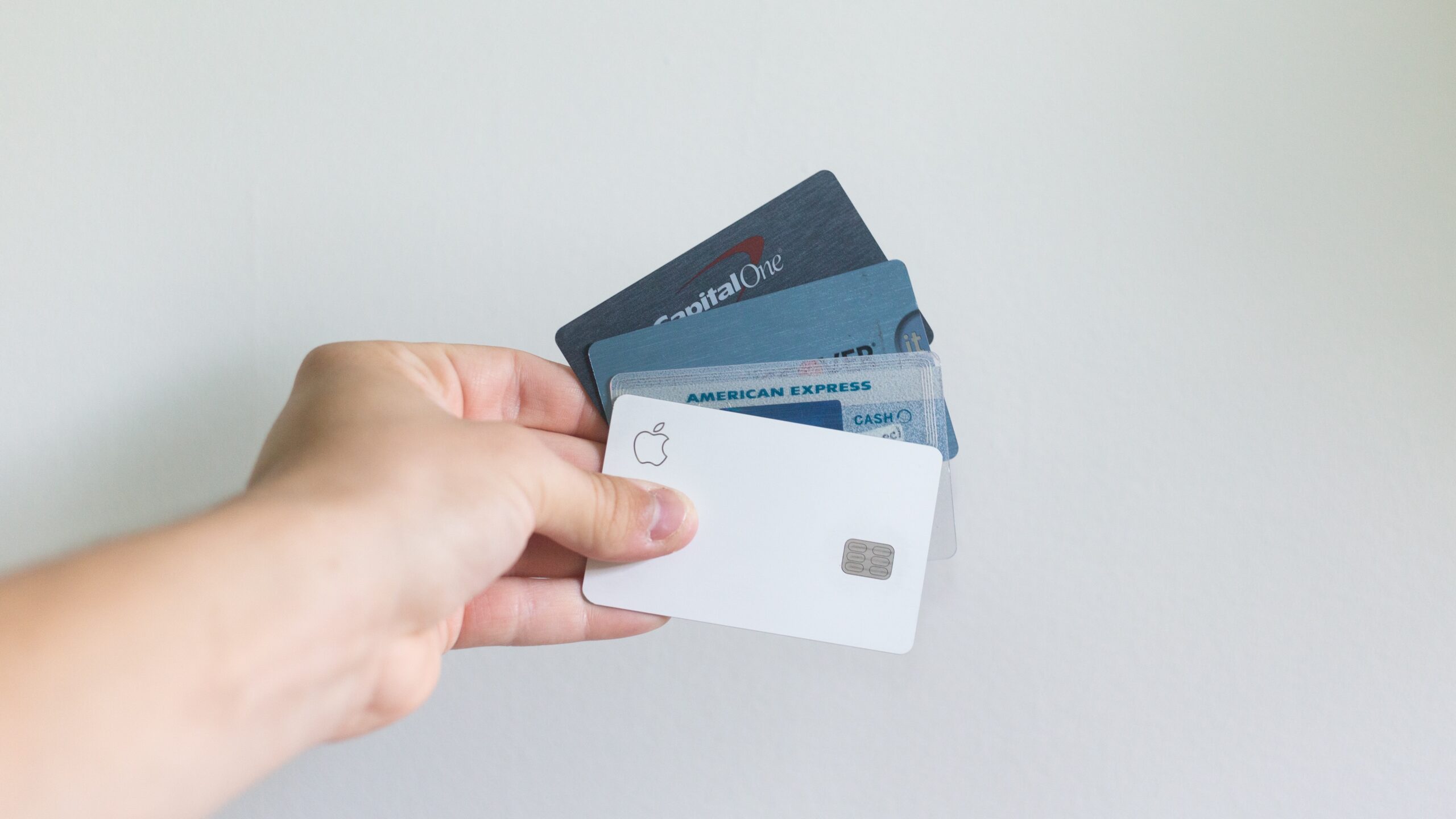 a hand holding four credit cards against a white background